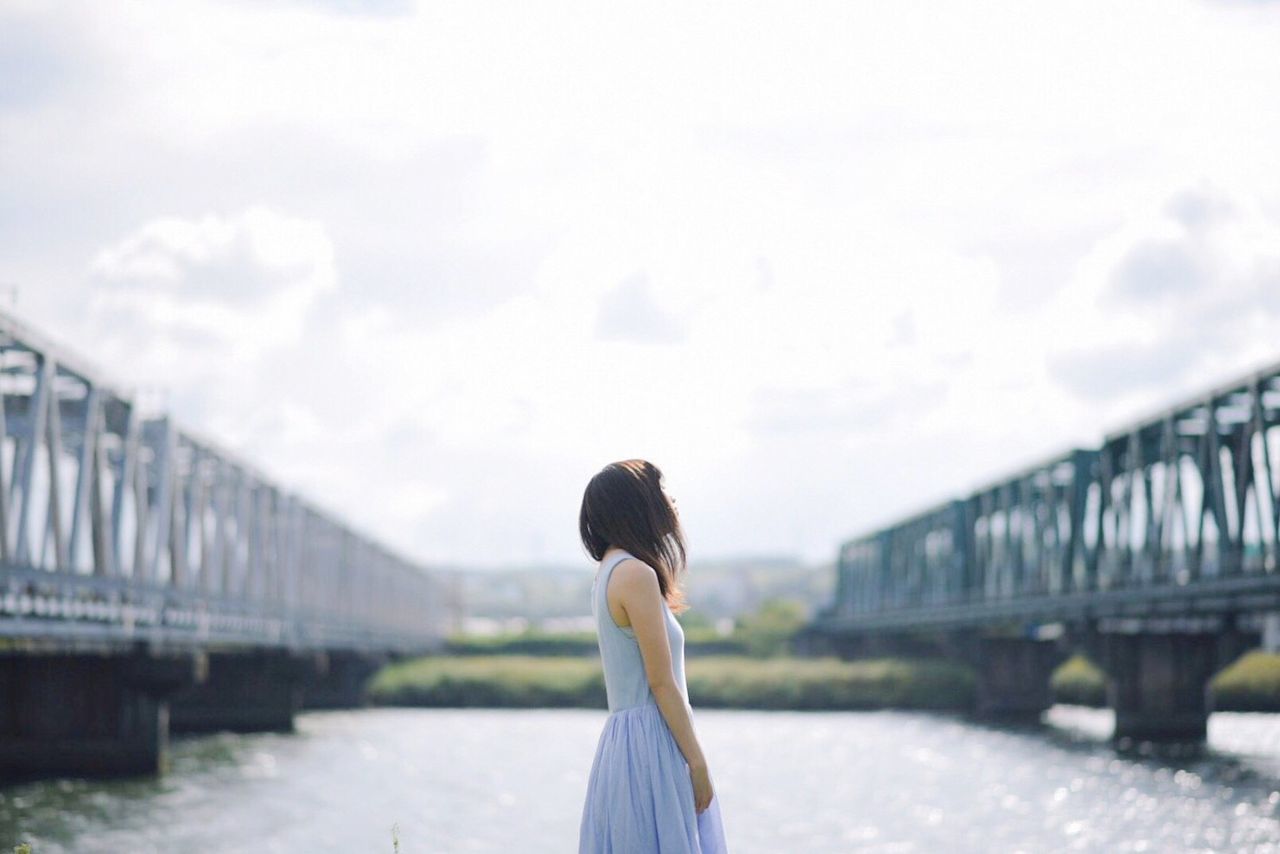 REAR VIEW OF WOMAN ON BRIDGE OVER WATER AGAINST SKY