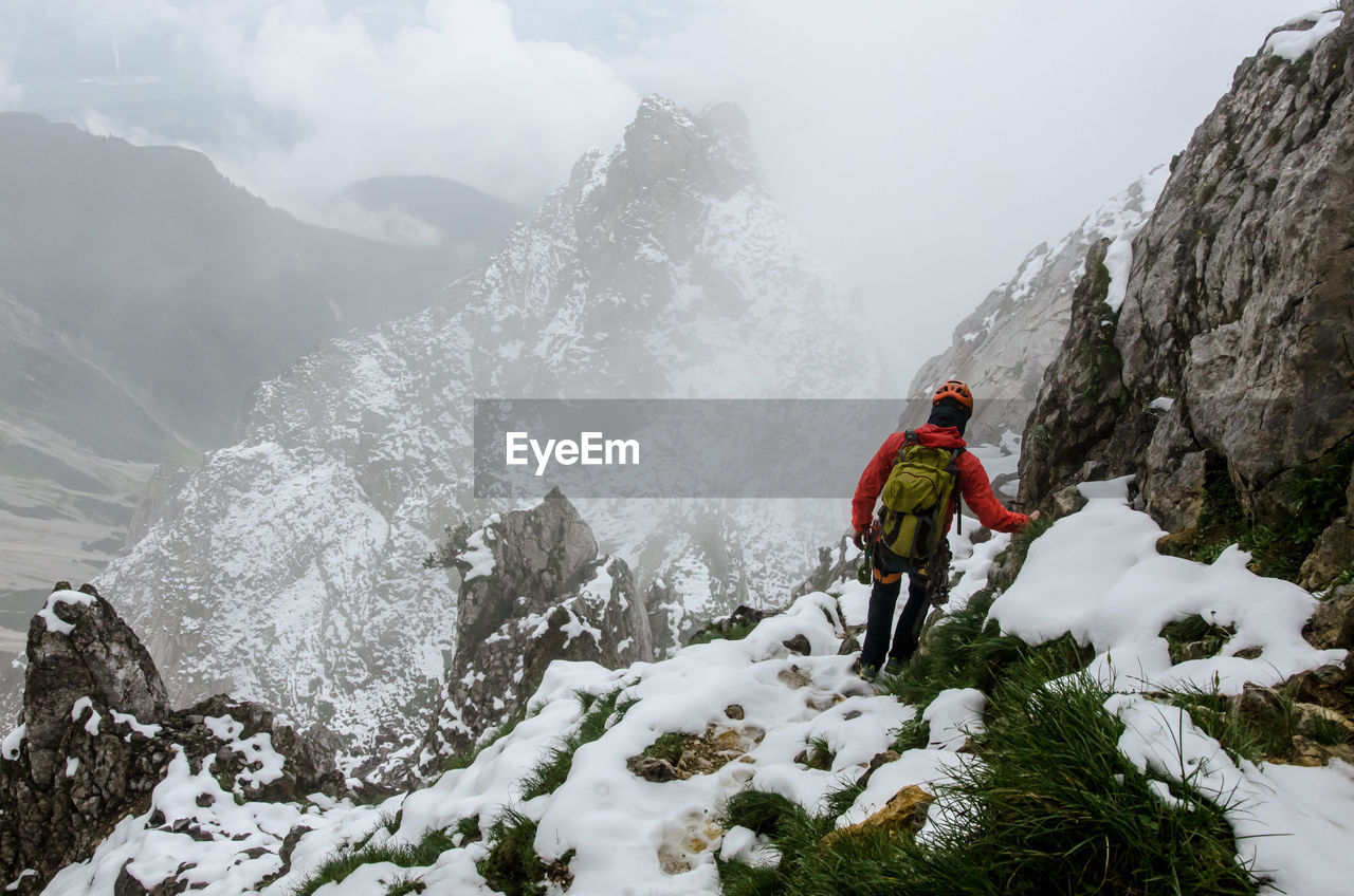 Rear view of hiker walking on snow covered mountain