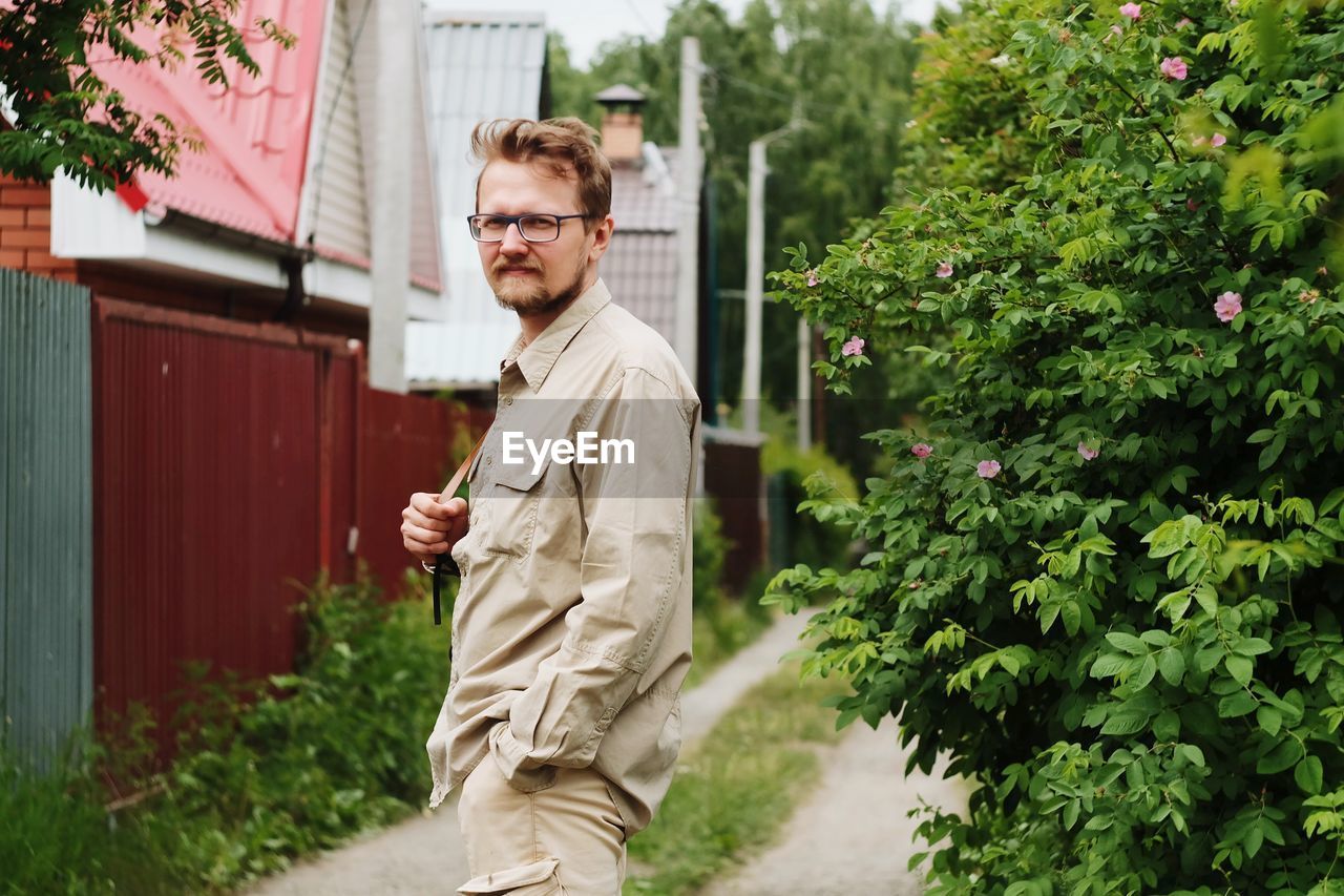 Portrait of man standing by plants against houses