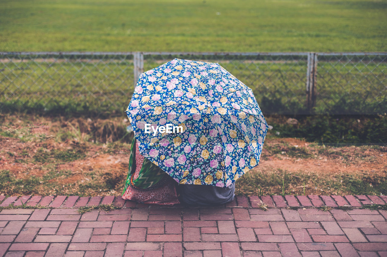 Rear view of couple sitting under umbrella on footpath against field