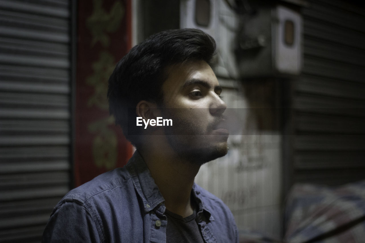 Young man exhaling smoke by shutter