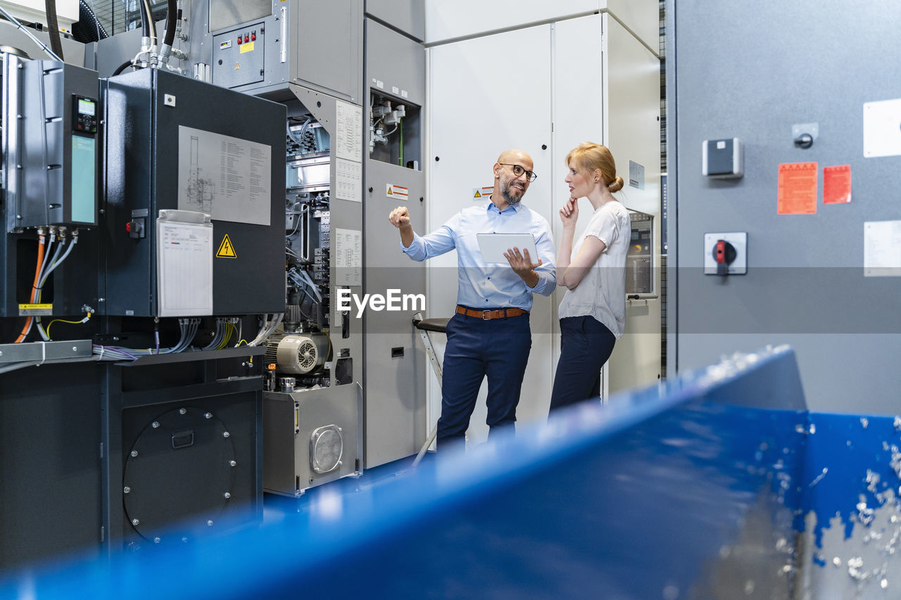 Businessman with tablet showing machine to businesswoman in factory