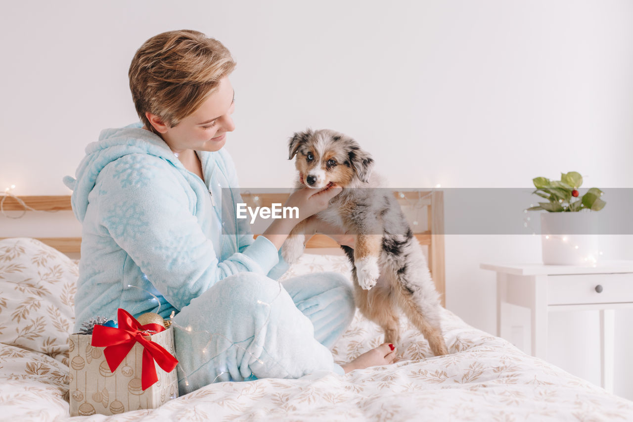 Young woman and dog sitting on bed at home