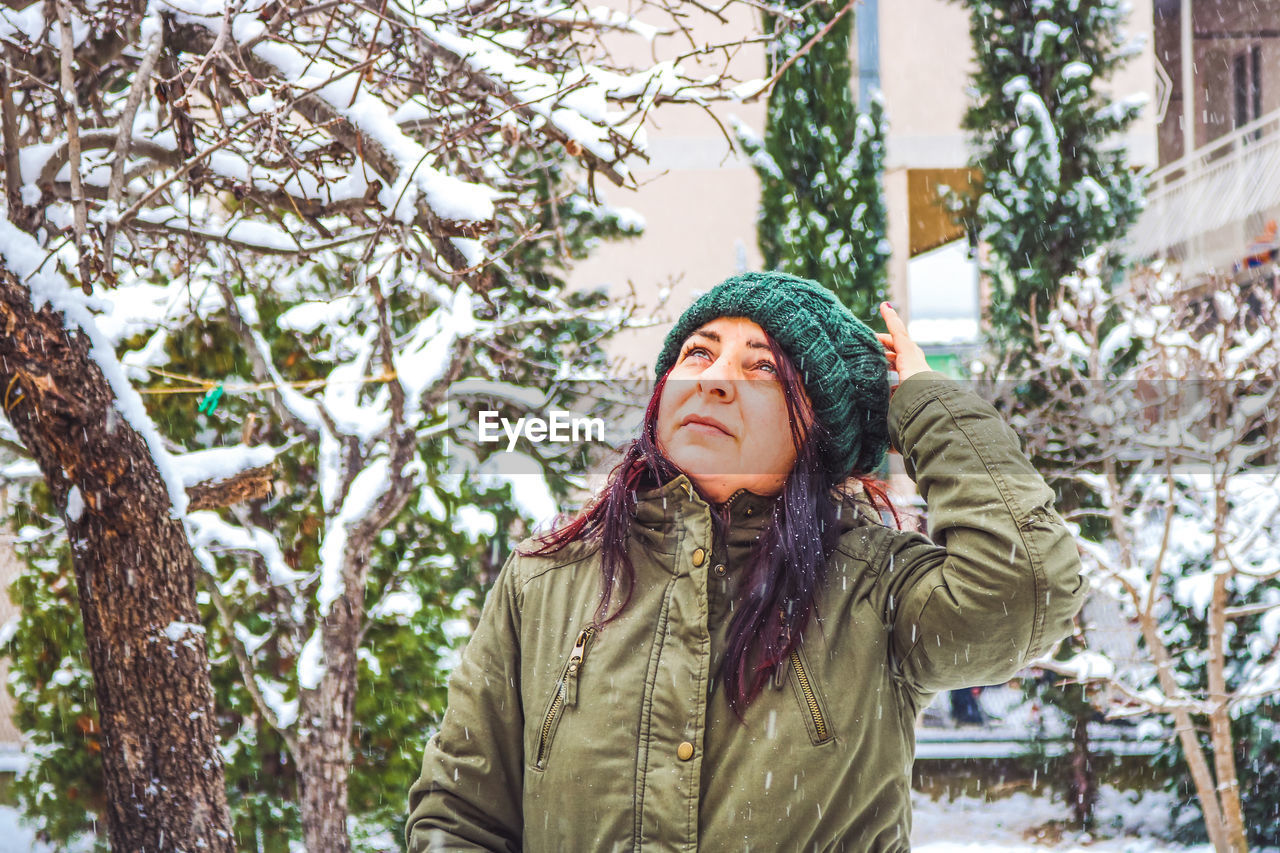 Woman looking away while standing against tree outdoors