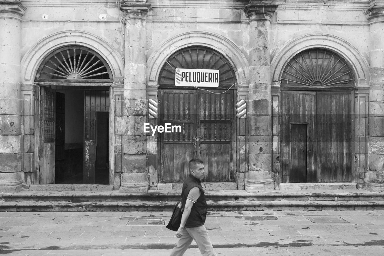 MAN WALKING IN FRONT OF BUILDING