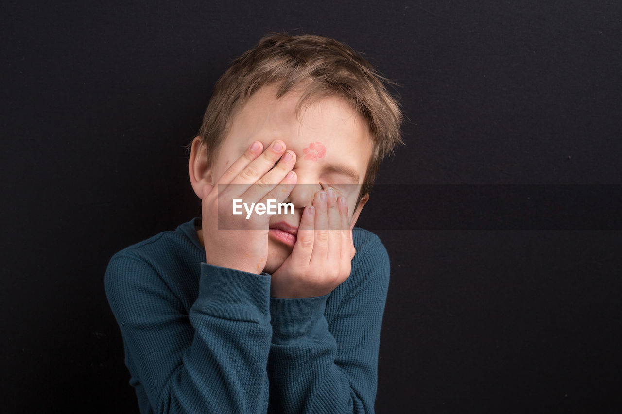 Close-up of man covering face against black background