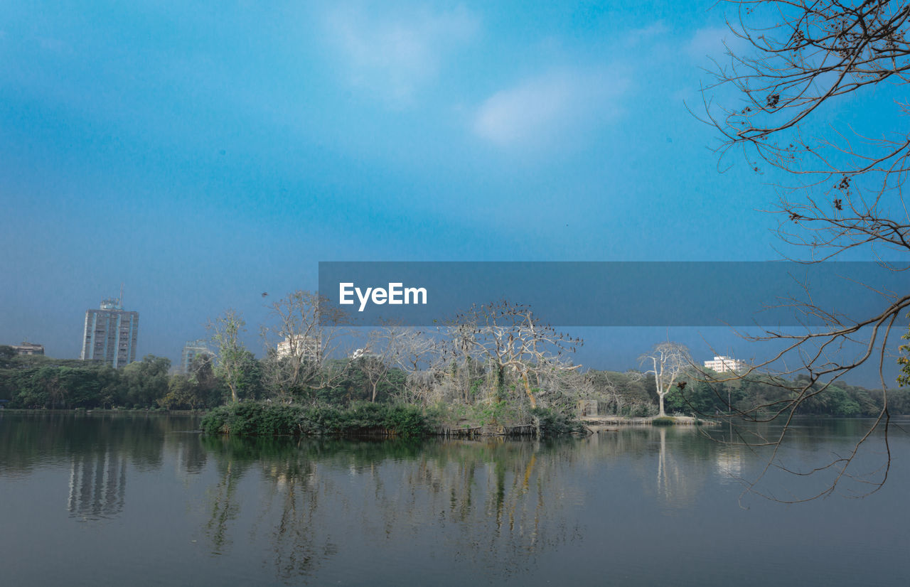 SCENIC VIEW OF LAKE BY TREES AND BUILDINGS AGAINST SKY