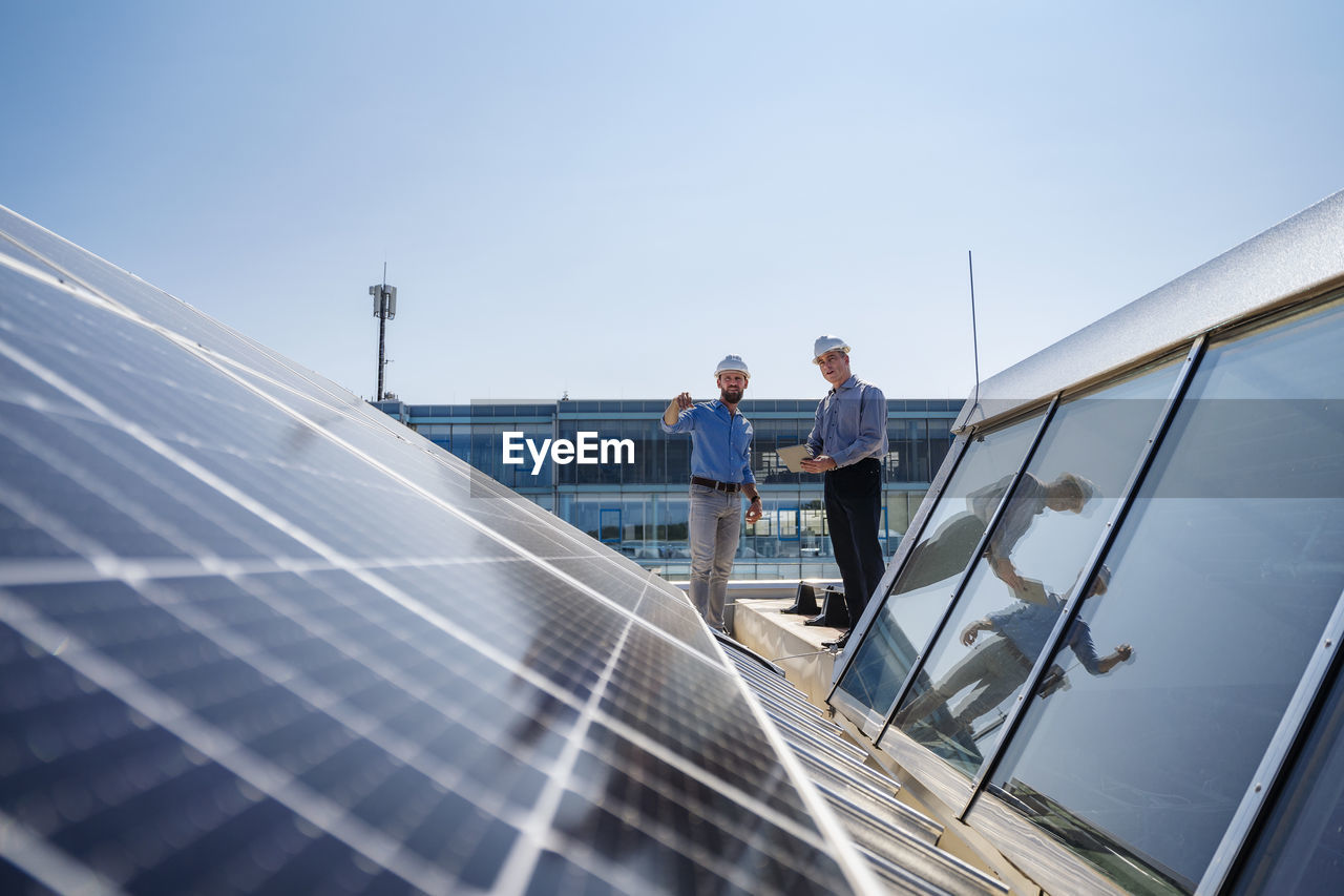 Two executives in hardhats discussing on the rooftop of a solar-powered company building