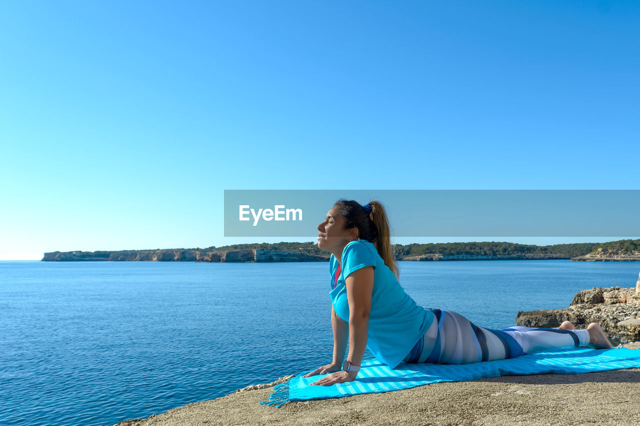 Middle-aged fitness woman outdoors in front of the sea does yoga stretching exercises