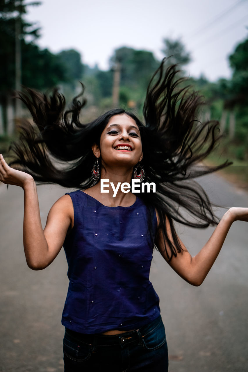 Smiling young woman tossing hair while standing on road