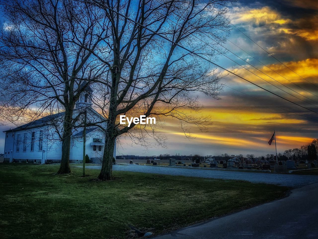 BARE TREES ON LANDSCAPE AGAINST SKY AT SUNSET