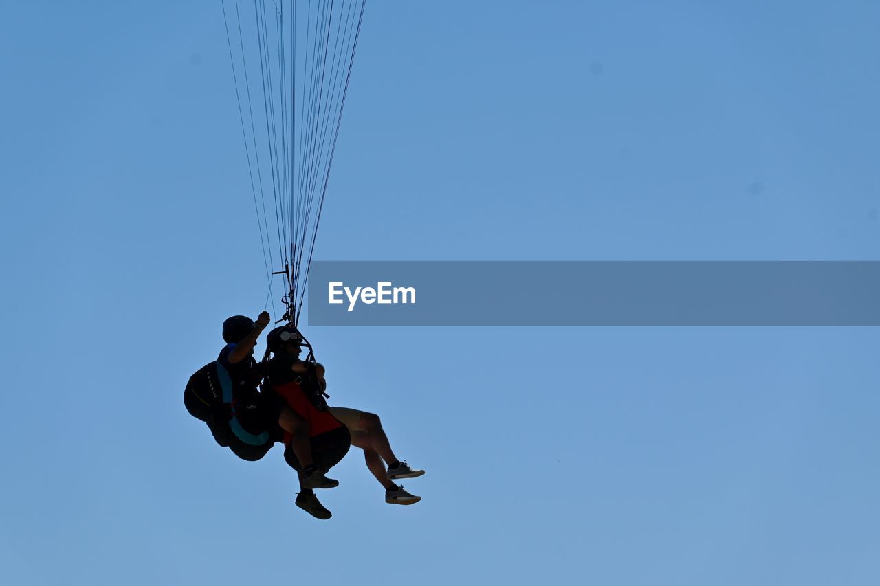 Low angle view of men paragliding against clear blue sky