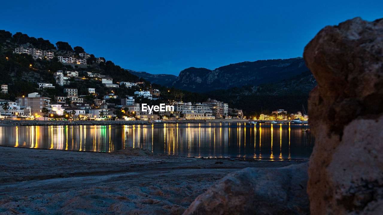 ILLUMINATED BUILDINGS BY SEA AGAINST SKY AT DUSK