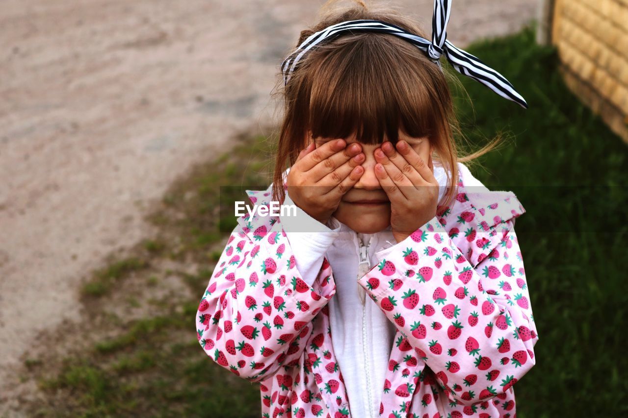 Cute girl with hands covering eyes standing on land