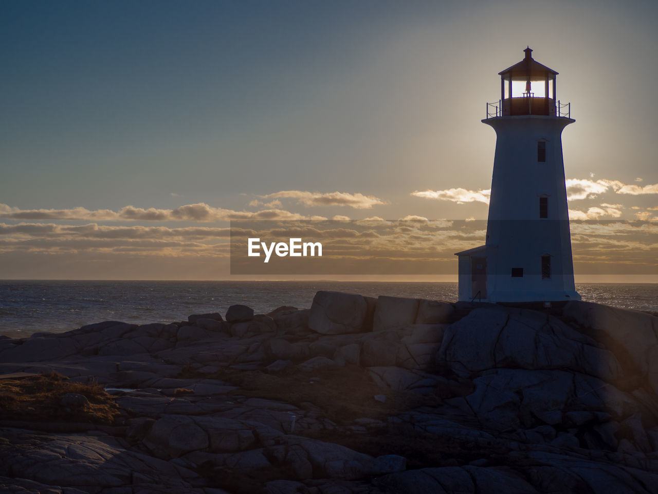 Lighthouse by sea against sky during sunset