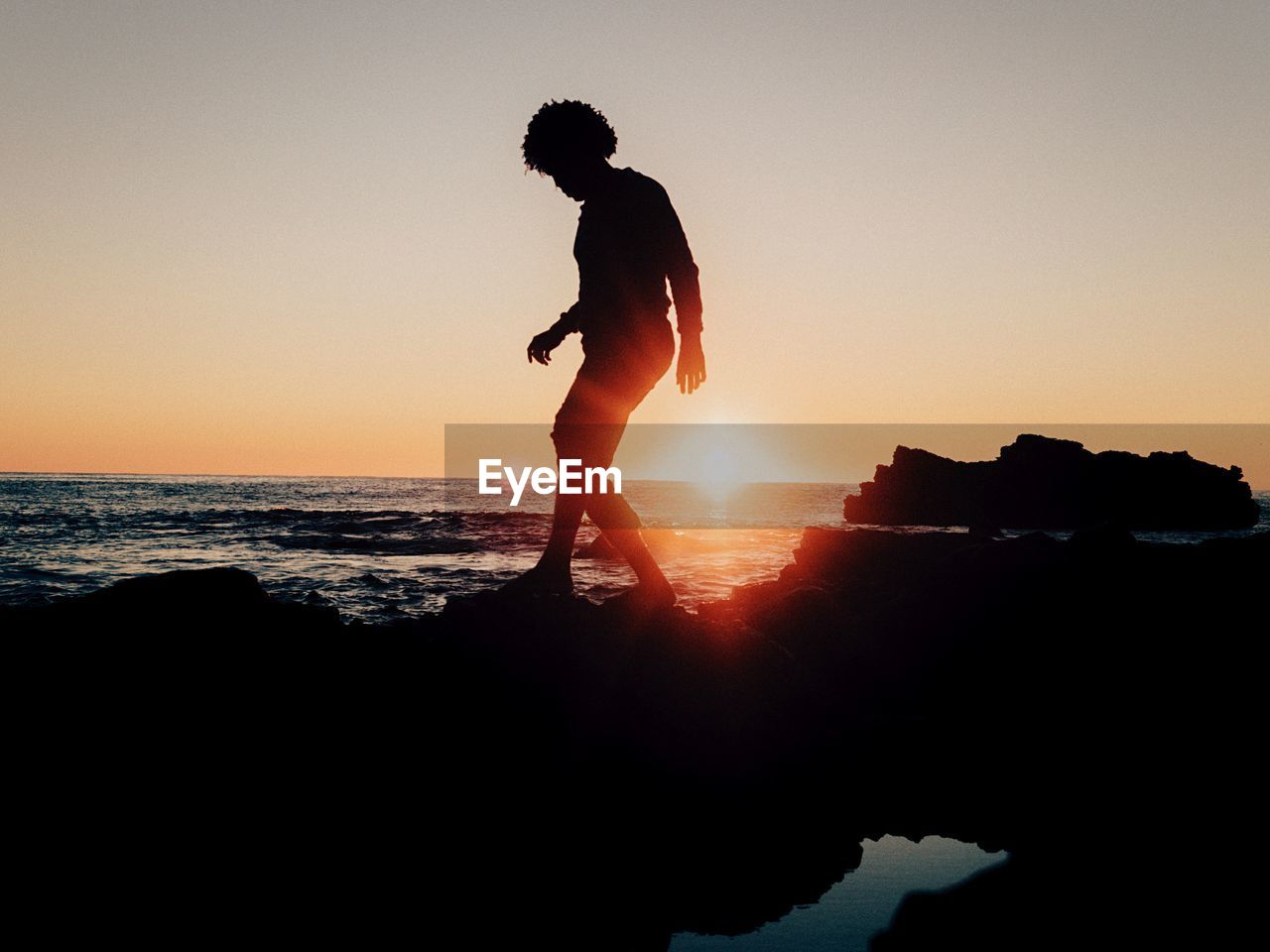 Silhouette person on rock formation by sea against clear sky during sunset