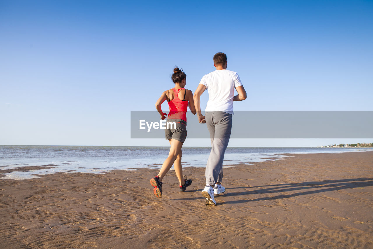 Full length of people on beach against clear sky