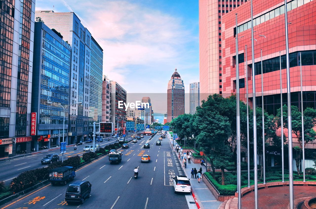 VEHICLES ON CITY STREET AMIDST BUILDINGS AGAINST SKY