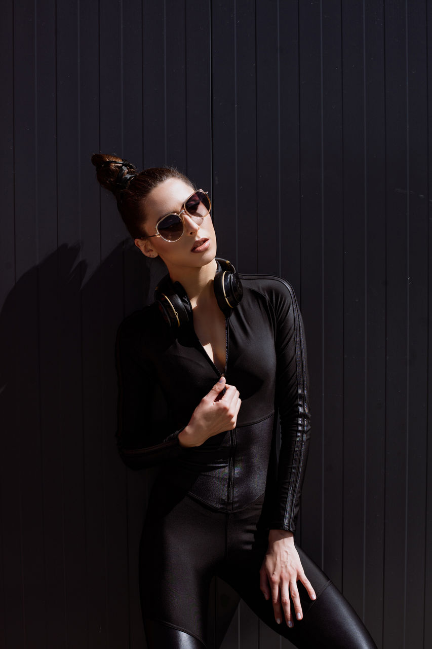 portrait of young woman wearing sunglasses while standing against wall