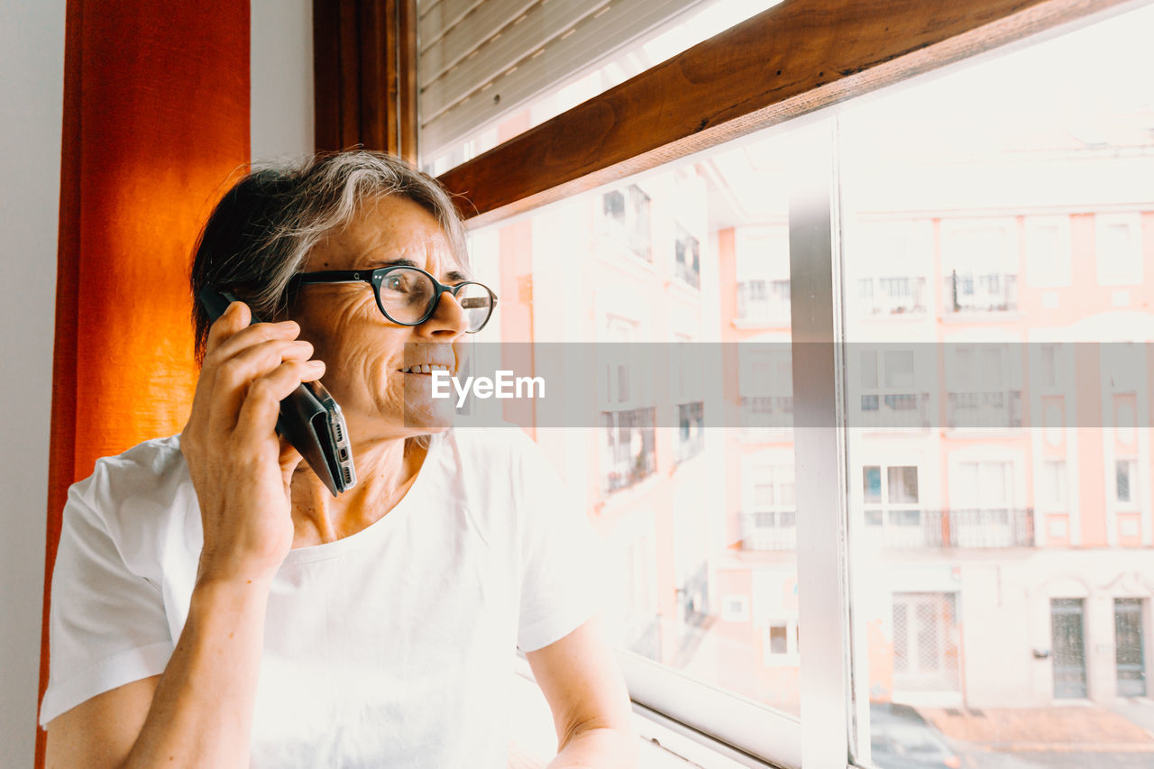 Mature woman talking on phone by window