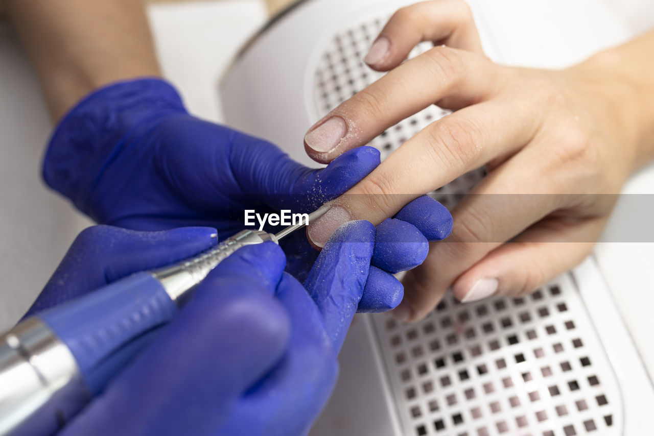 The manicurist cuts the cuticles of the nails with an electric milling machine wearing blue latex