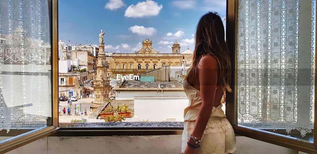 WOMAN STANDING BY WINDOW IN FRONT OF BUILDING