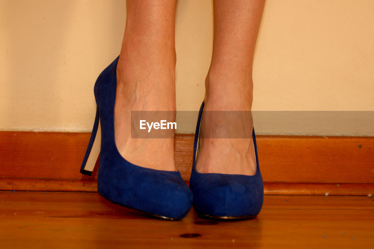 LOW SECTION OF WOMAN WEARING SHOES STANDING ON HARDWOOD FLOOR