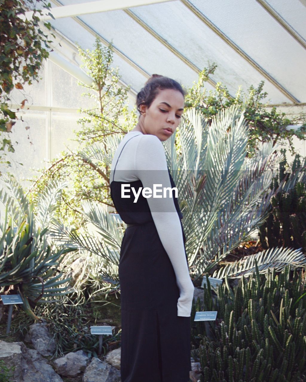 YOUNG WOMAN STANDING AGAINST PLANTS