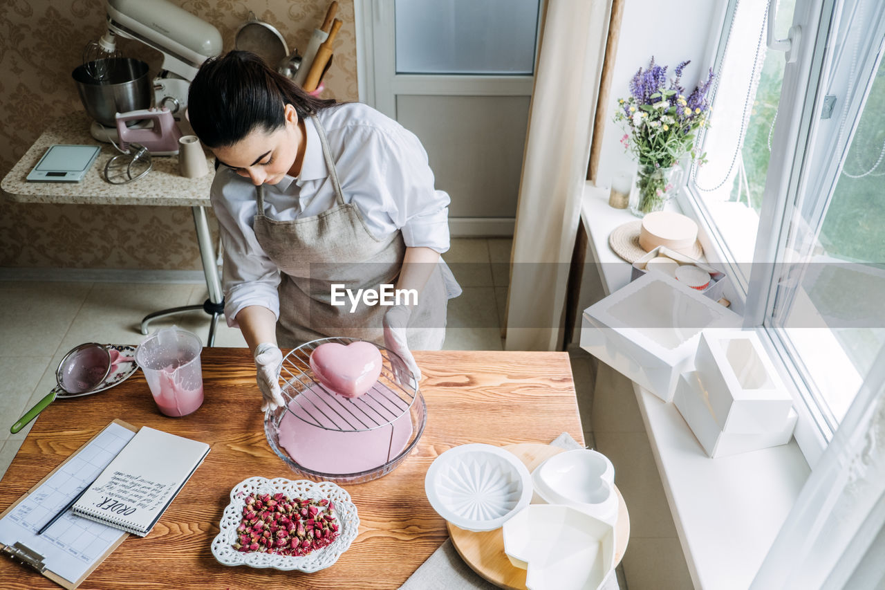 Female baker make perfect custom pink heart shape cake in kitchen bakery. online cake store. custom