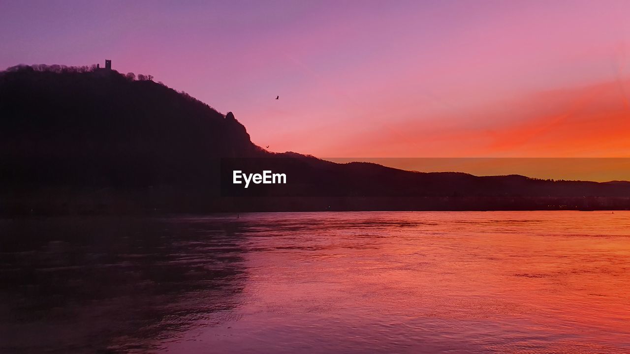 SCENIC VIEW OF SEA AND SILHOUETTE MOUNTAINS AGAINST SKY DURING SUNSET