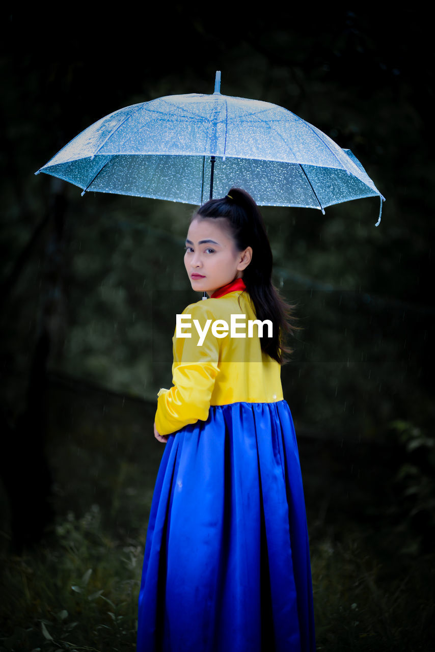 Portrait of woman with umbrella standing in forest