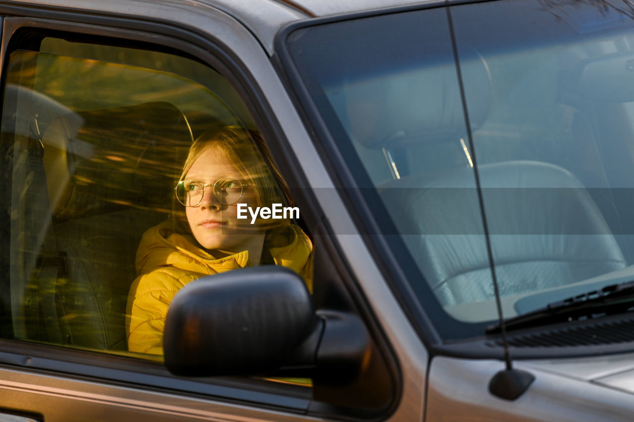 Boy sitting in car looking out passanger window tword setting sun