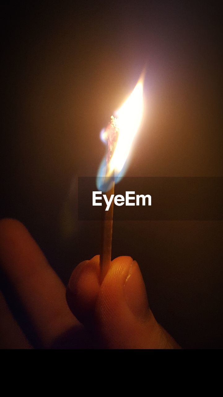Close-up of hand holding illuminated matchstick in darkroom