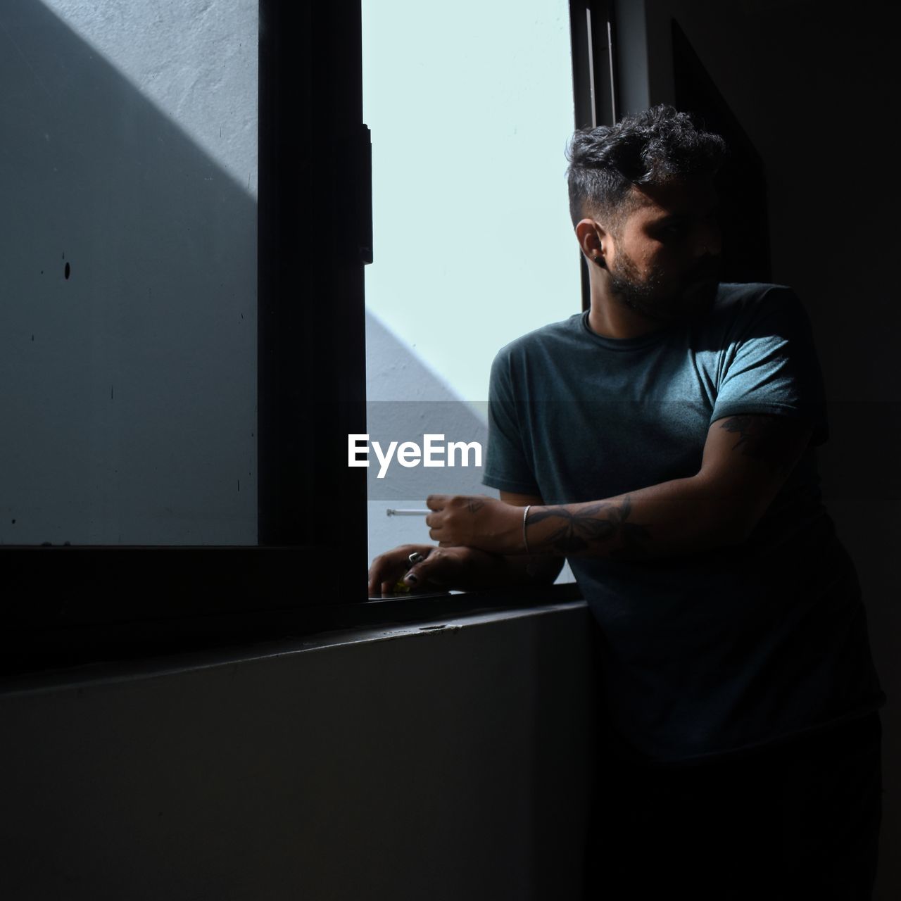 side view of young man looking through window at home