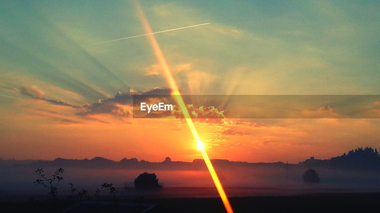 SUN SHINING THROUGH CLOUDS OVER LANDSCAPE