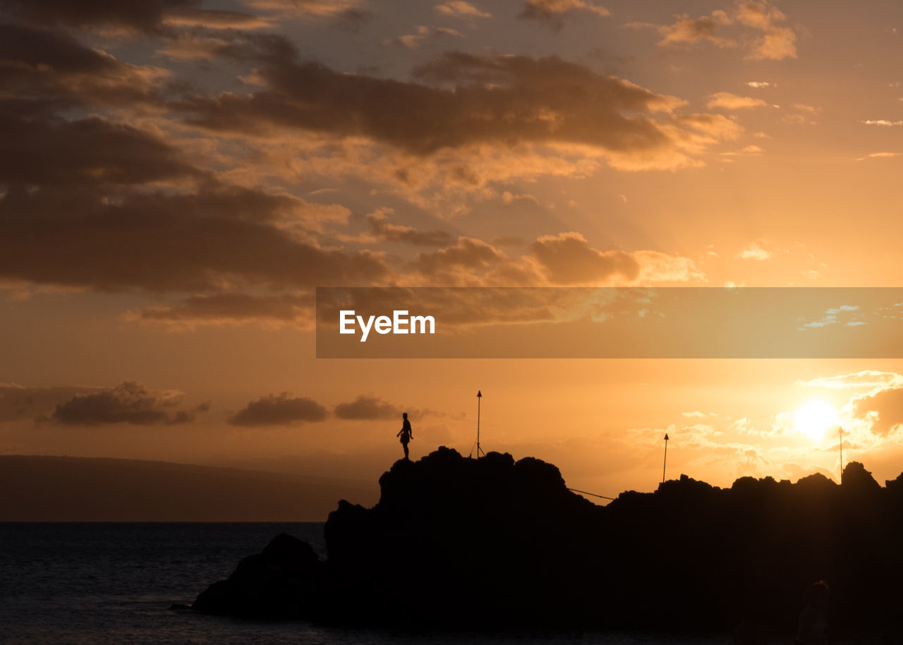 Silhouette rocks by sea against sky during sunset