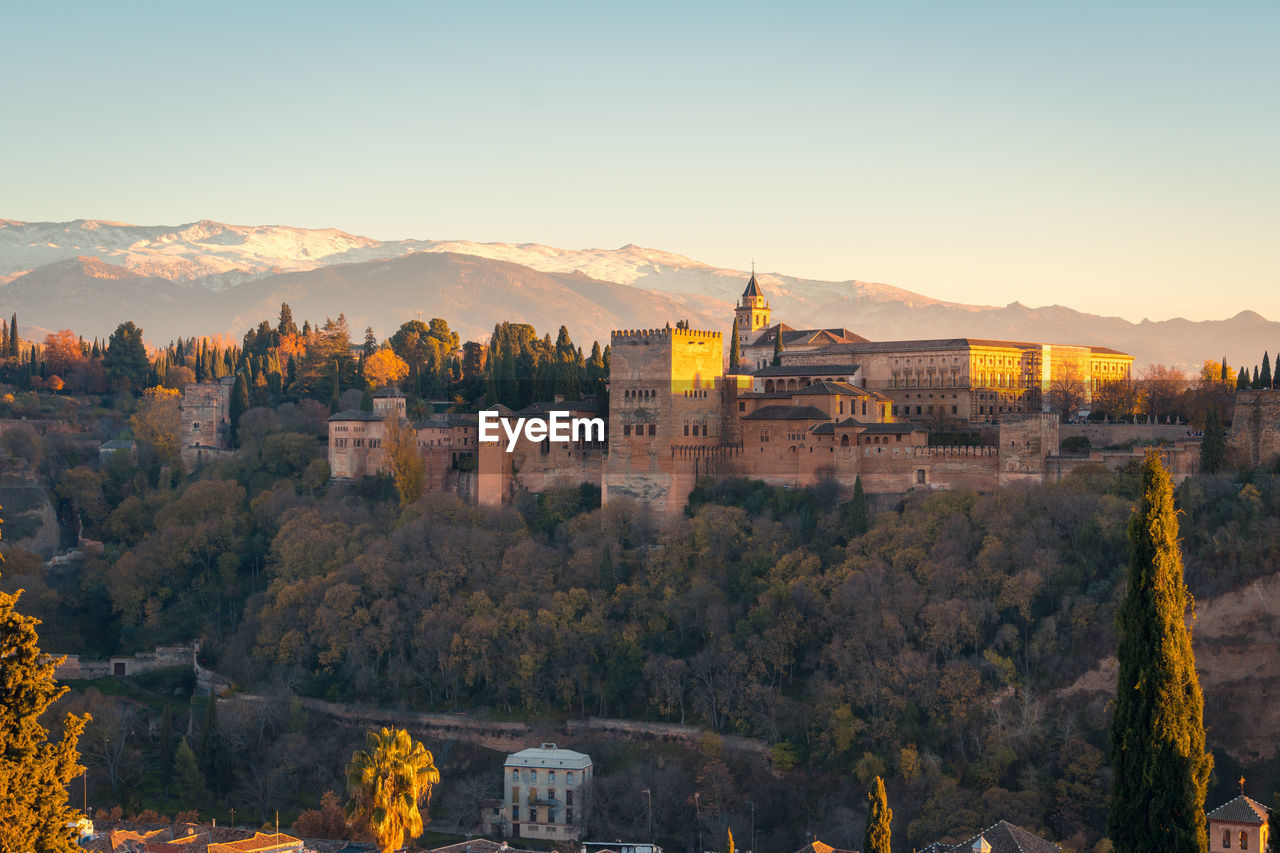 Breathtaking view of sunlit alhambra fortress complex located on lush hill near mountain range at sunrise in granada, spain