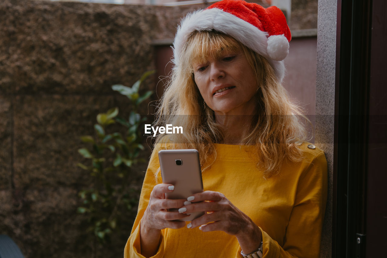 Woman at home with santa claus hat and mobile phone