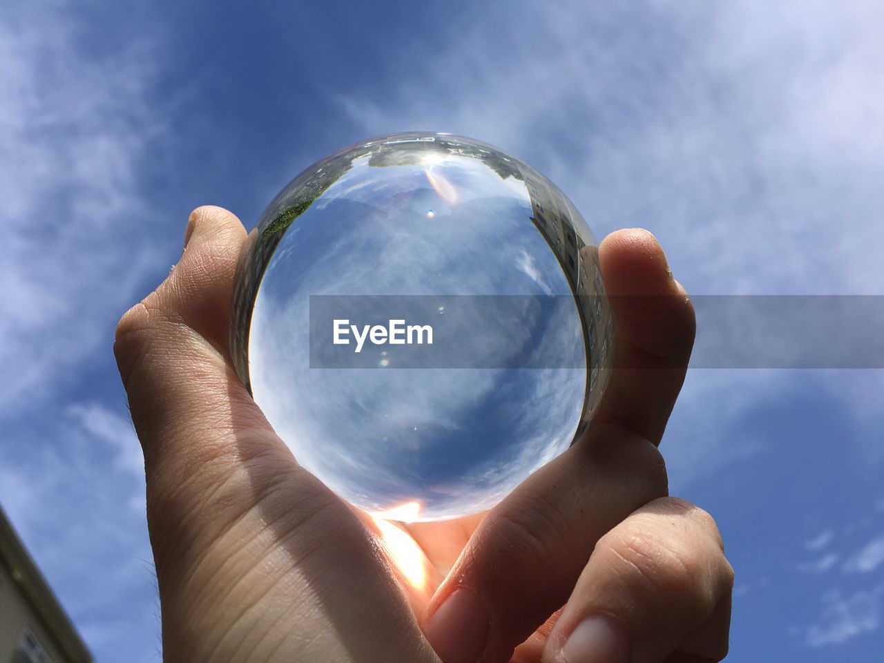 Close-up of hand holding crystal ball against sky