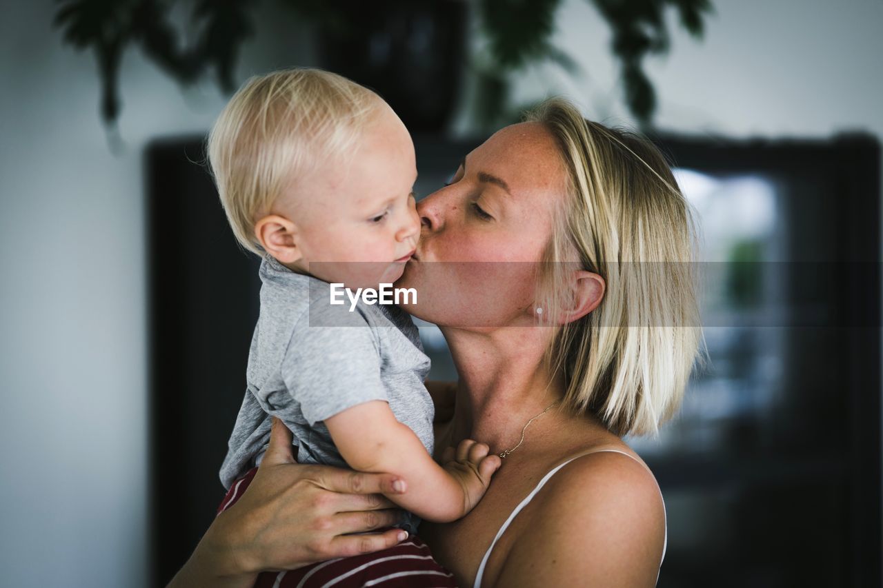 Close-up of mother kissing baby boy at home