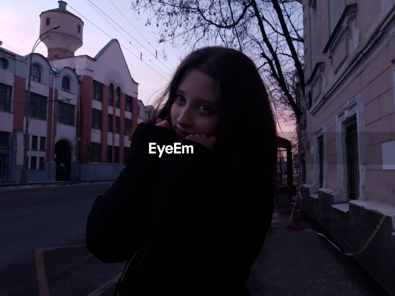 Portrait of woman standing on street in city at sunset