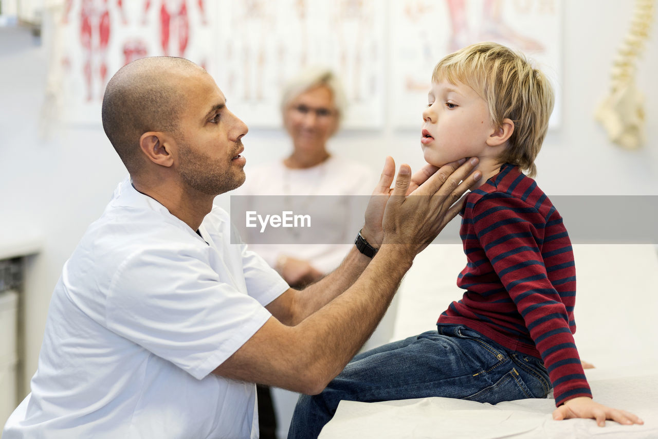 Side view of male doctor checking boy's throat at clinic