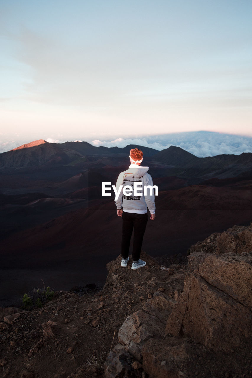 FULL LENGTH OF MAN STANDING ON ROCK AGAINST MOUNTAIN