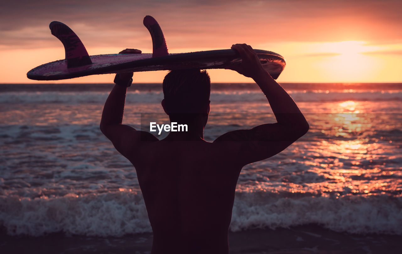 Close-up of man carrying surfboard on head while standing at beach