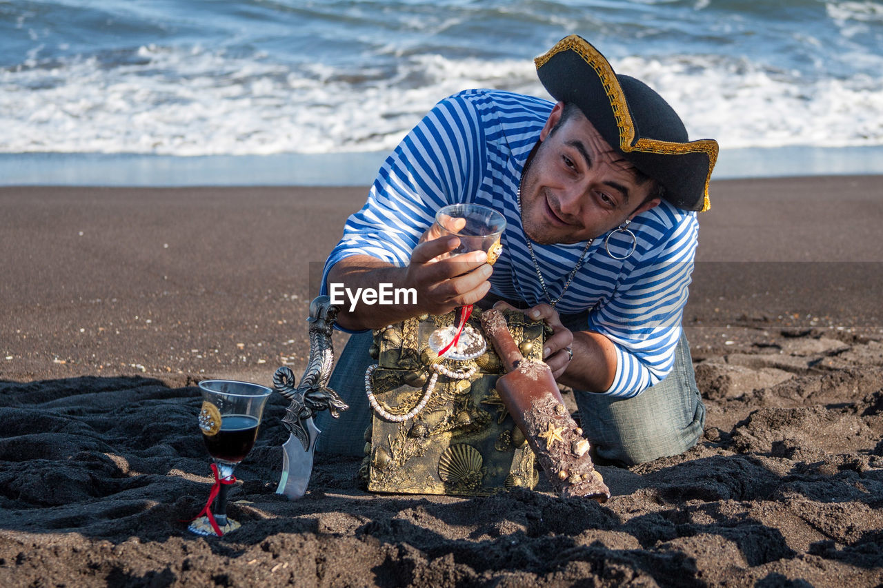 Pirate holding wineglass with treasure chest at beach