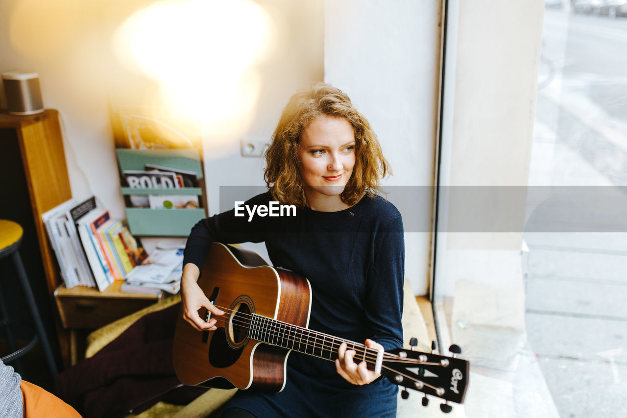 High angle view of young woman playing guitar by window at home