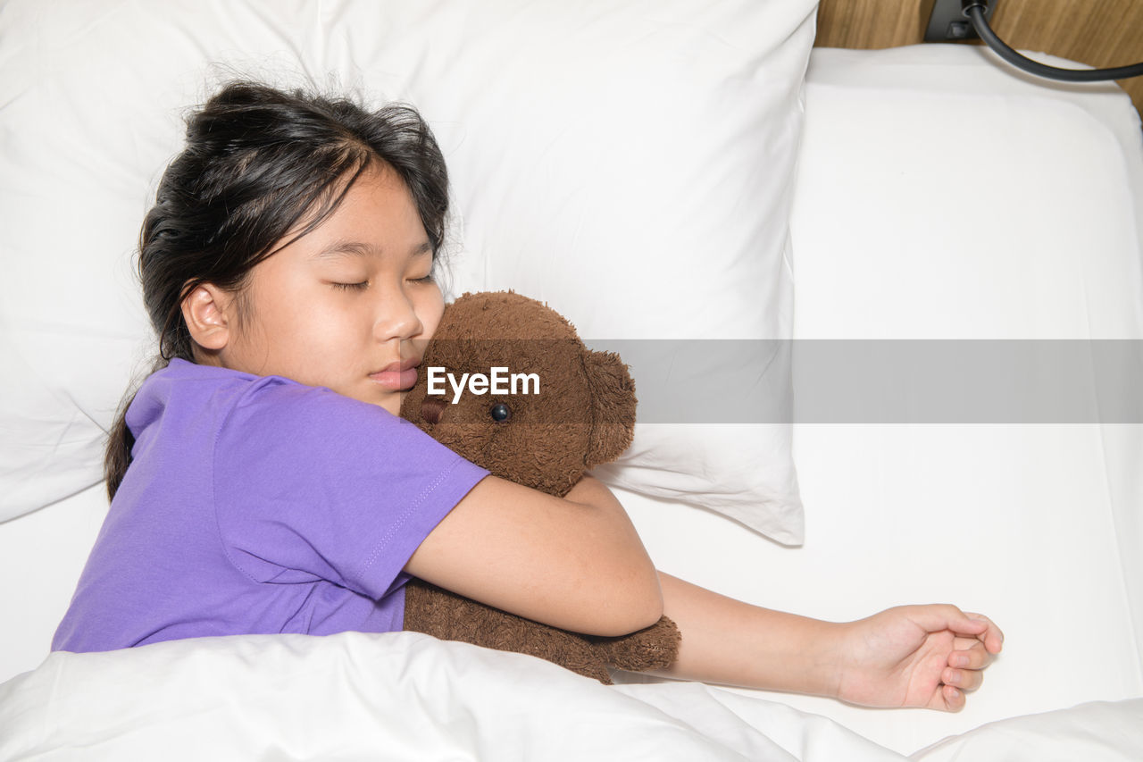 Child little girl sleeps with a toy teddy bear in the bed,