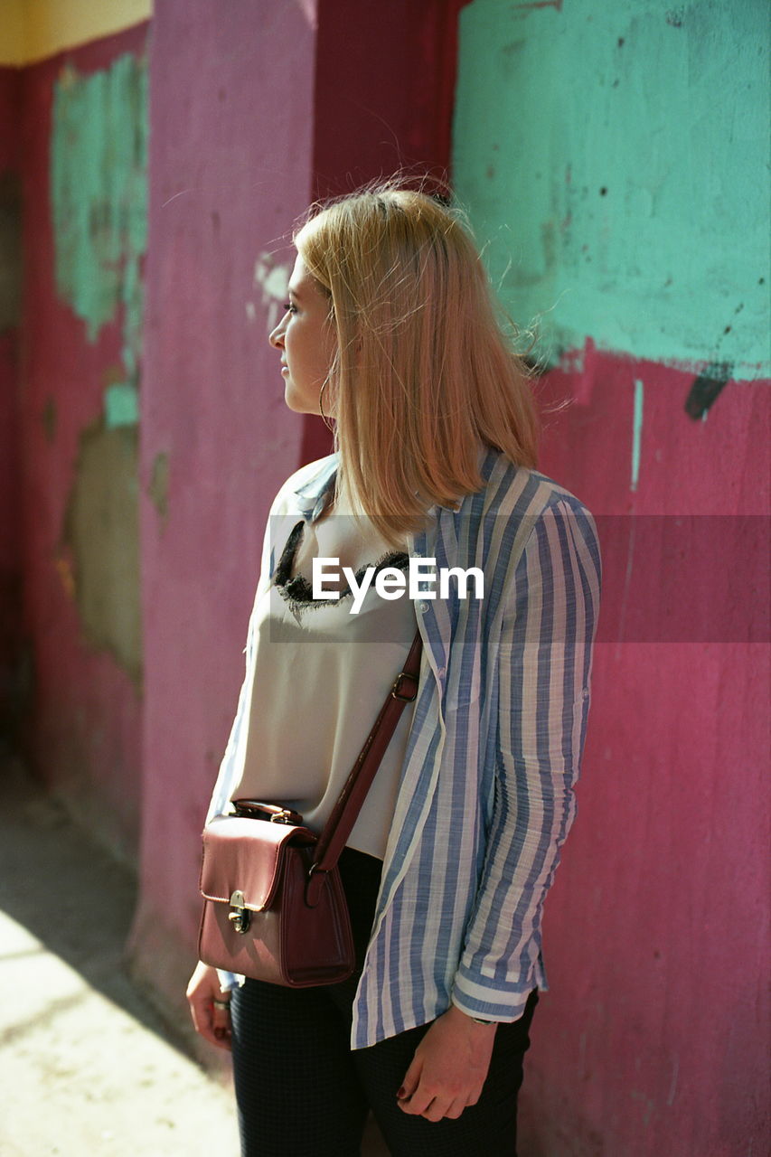 Woman looking away while standing against wall