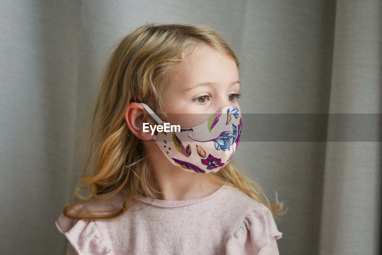 Close-up of cute girl wearing mask standing at home