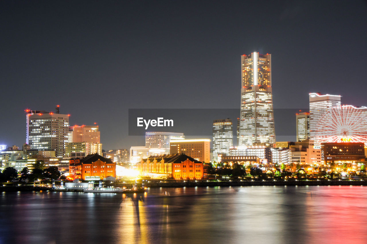 Illuminated buildings by river against sky at night